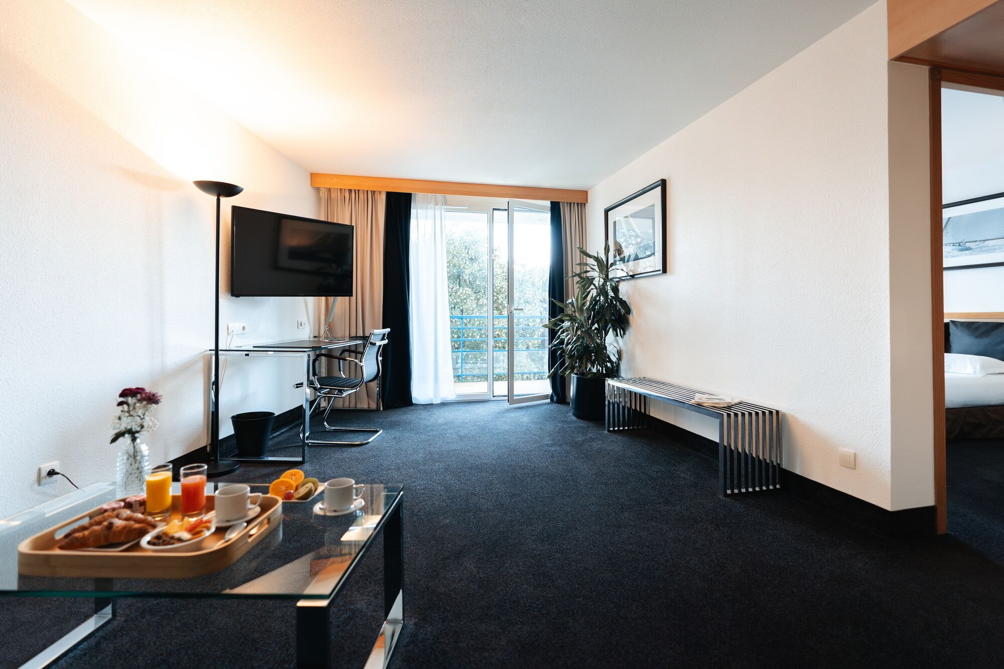 Una habitación de hotel con cama, escritorio con desayuno, televisor y ventana grande.