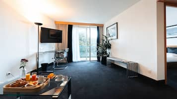 Quarto de hotel com cama, secretária com café da manhã, televisão e uma janela grande.