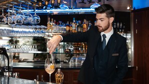 Un barman prépare un cocktail dans un bar, avec une variété de bouteilles et de verres en arrière-plan.