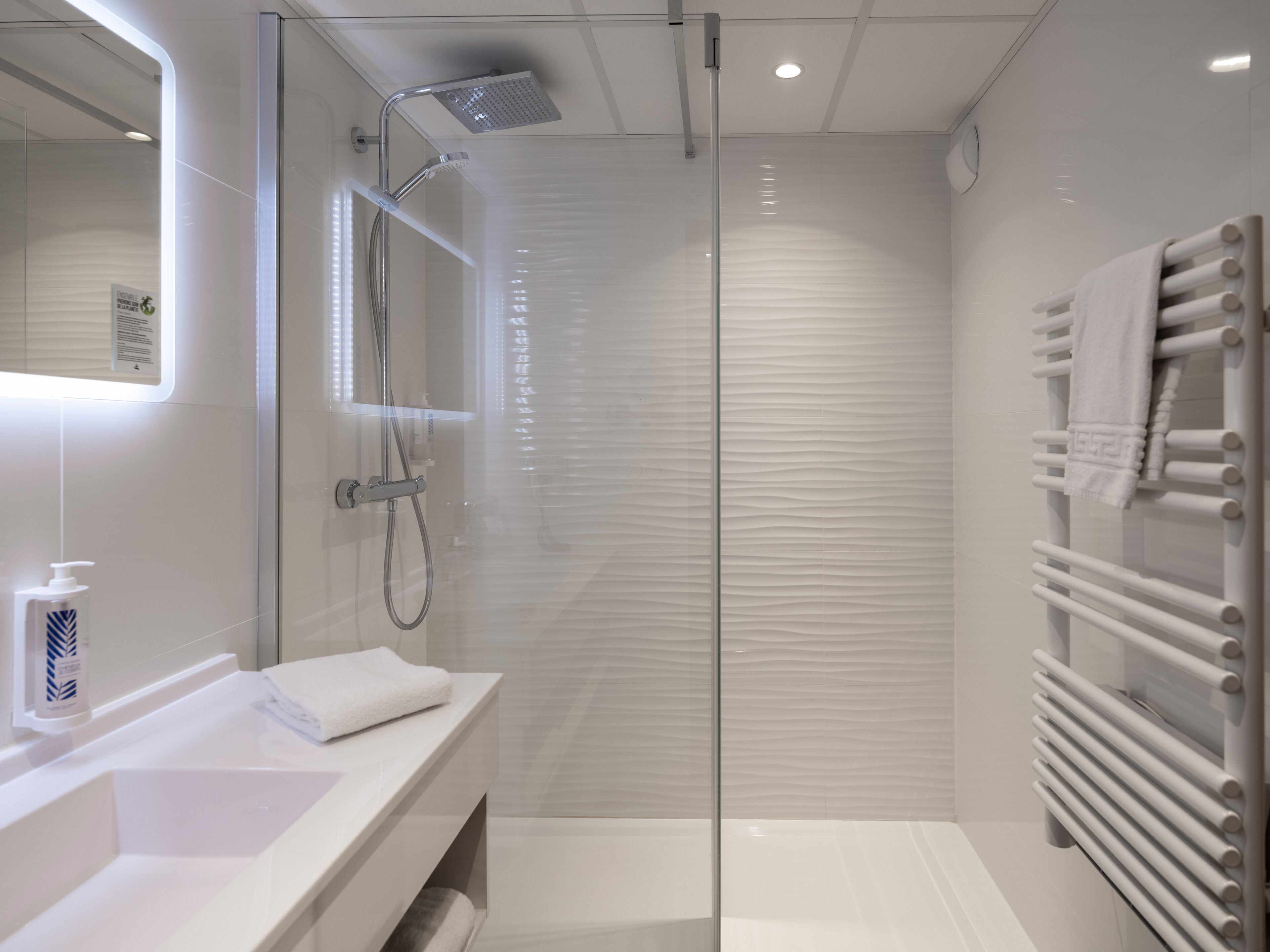 A modern bathroom with a glass-enclosed shower, a white sink, and a towel rack.