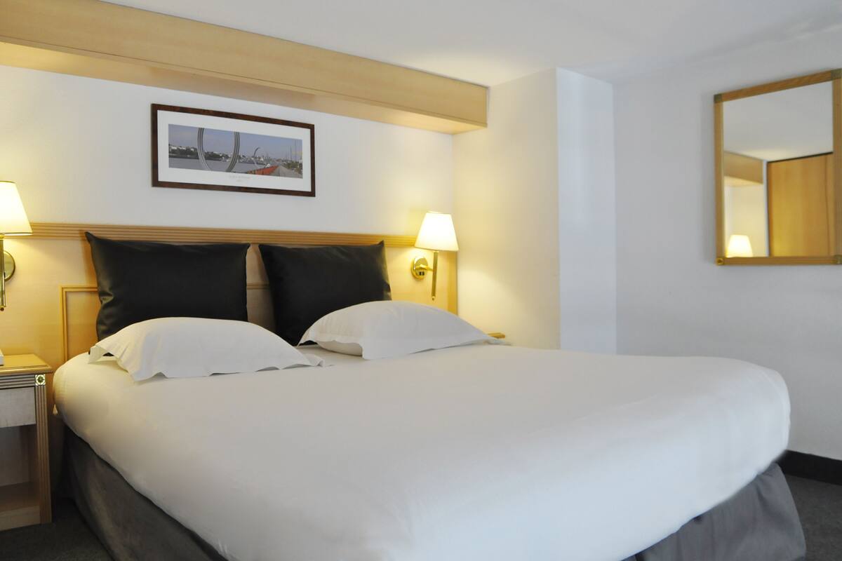 A hotel room with a large bed, two bedside lamps, a framed picture on the wall, and a mirror.