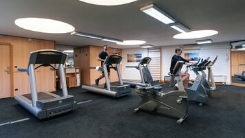 Une salle de sport équipée de tapis de course et de vélos elliptiques, de casiers en bois et d’un sol recouvert de moquette.