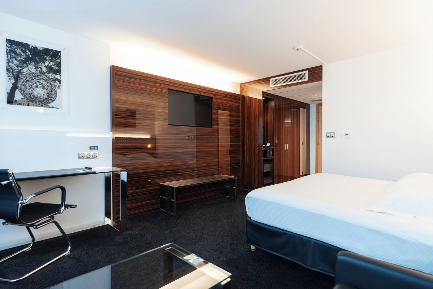 Ein modernes Hotelzimmer mit Bett, Schreibtisch, Stuhl, Fernseher und Kleiderschrank.