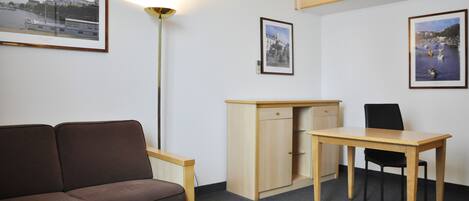 Una habitación pequeña con un sofá marrón, un escritorio de madera, una silla y una cama litera.