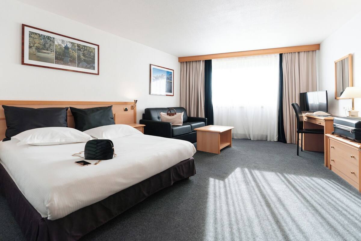 A hotel room with a large bed, a desk with a chair, a sofa, and a TV.