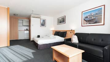 A hotel room with a bed, a sofa, a small wooden table, a kitchenette, and a bathroom.
