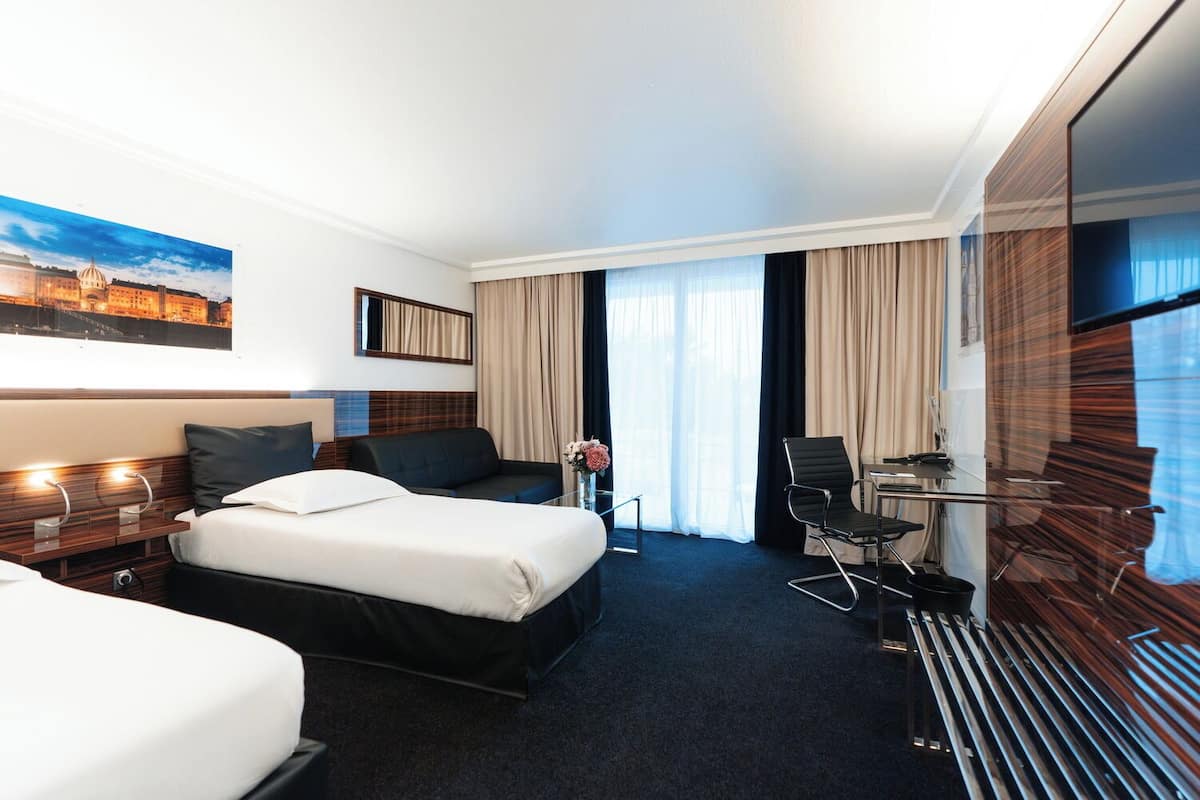 A hotel room with two beds, a desk, a chair, a TV, and a painting on the wall.