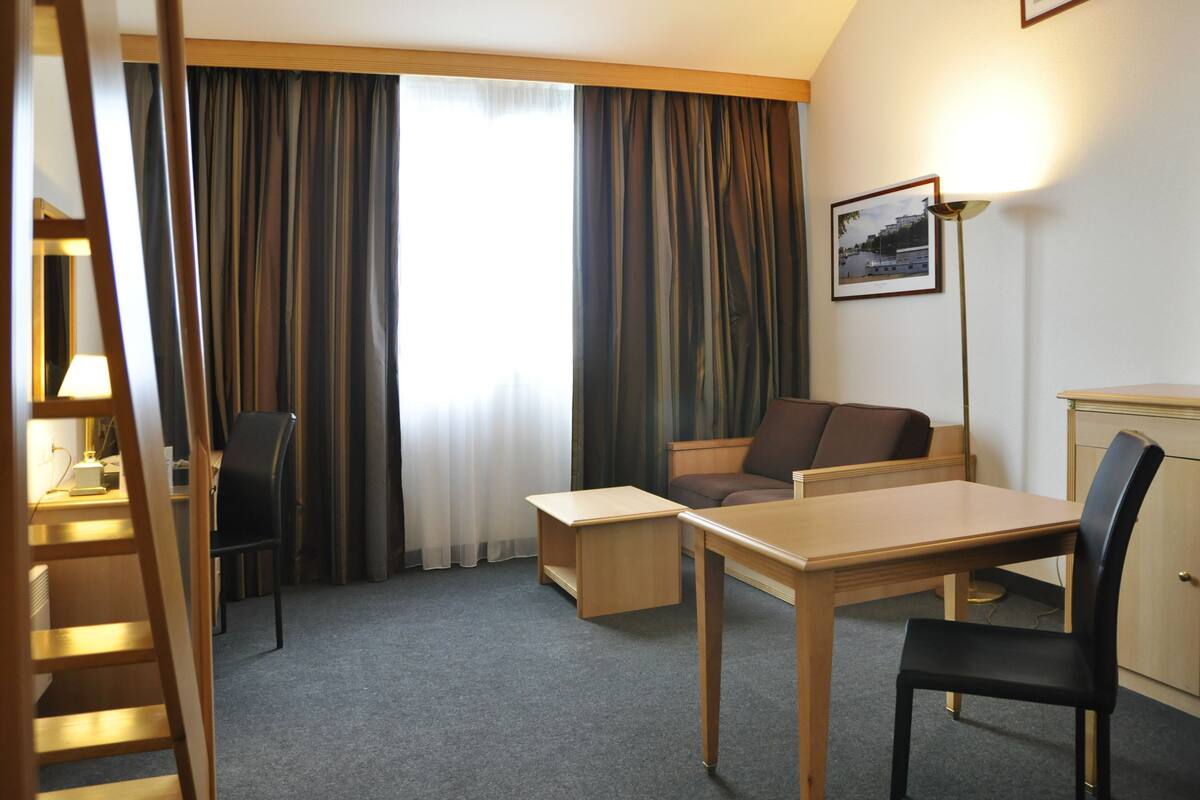 A hotel room with a desk, chair, sofa, and a lamp.