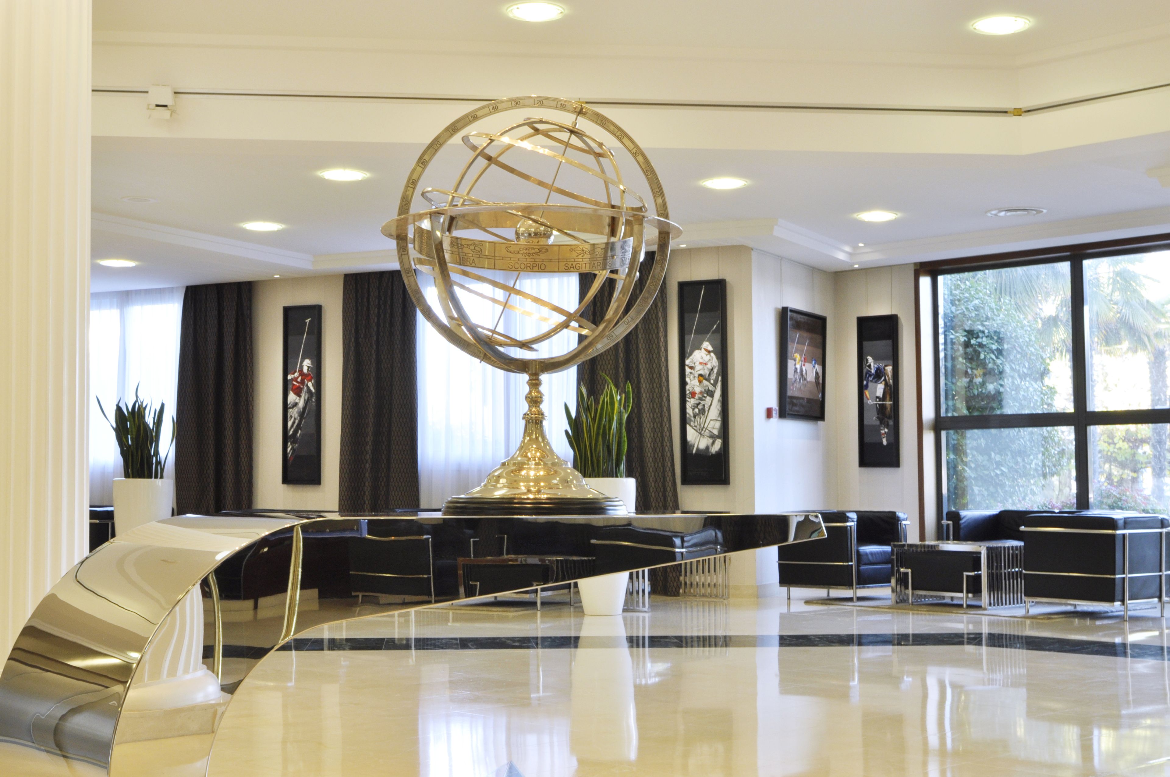 Een moderne lobby met een grote globe sculptuur, zwarte lederen zitplaatsen en grote ramen met uitzicht op groen.