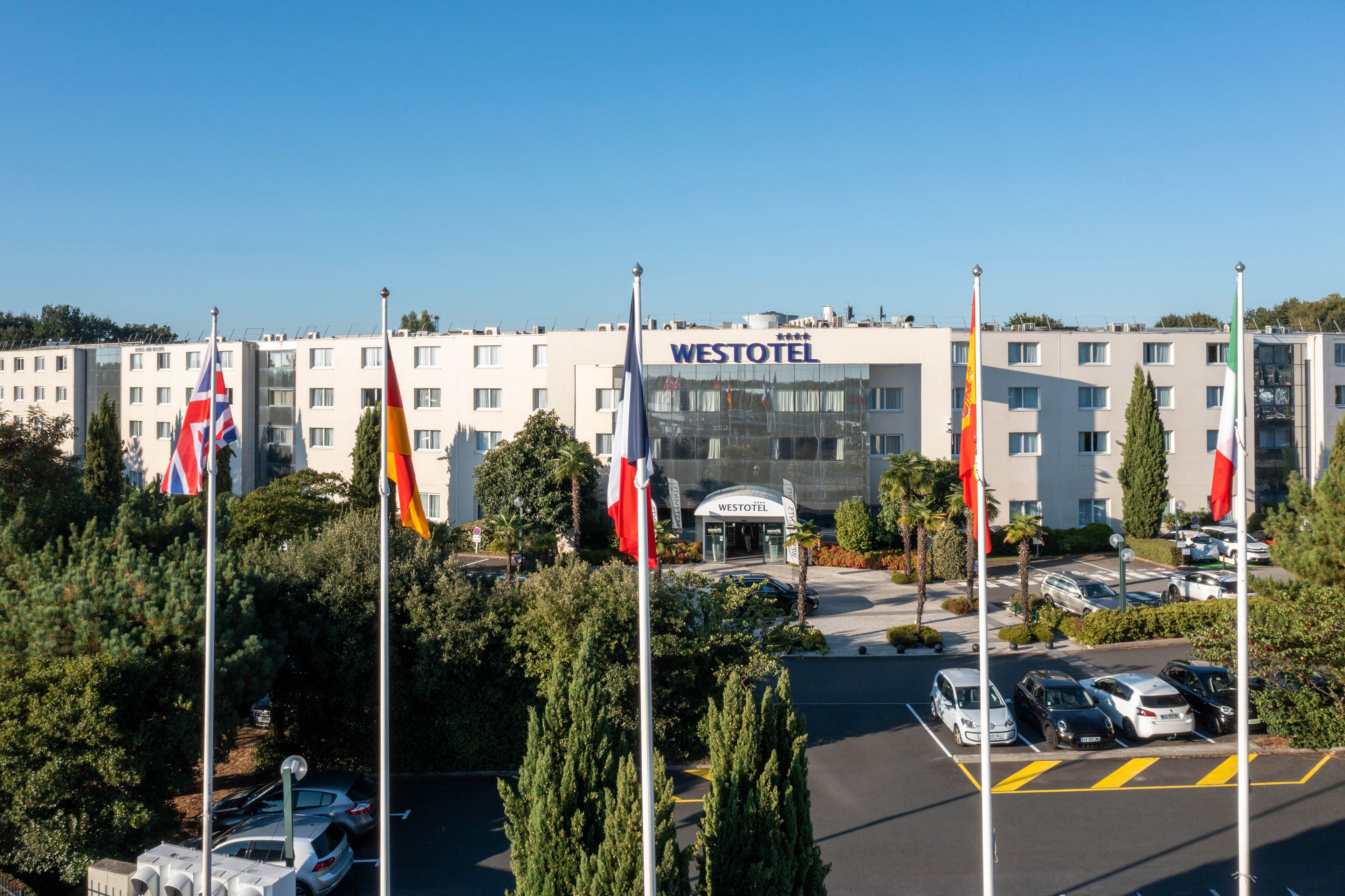 A Westotel hotel with multiple flags, a parking lot, and a clear sky.