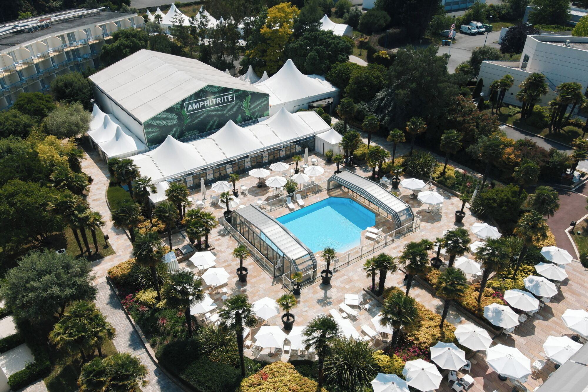 An aerial view of a hotel with a swimming pool surrounded by outdoor seating areas and palm trees.