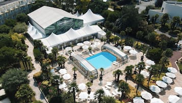 An aerial view of a hotel with a swimming pool surrounded by outdoor seating areas and palm trees.