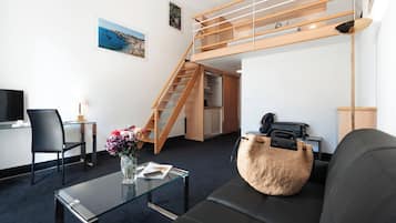 A compact living space with a loft bed, a desk with a chair, a sofa, and a coffee table.