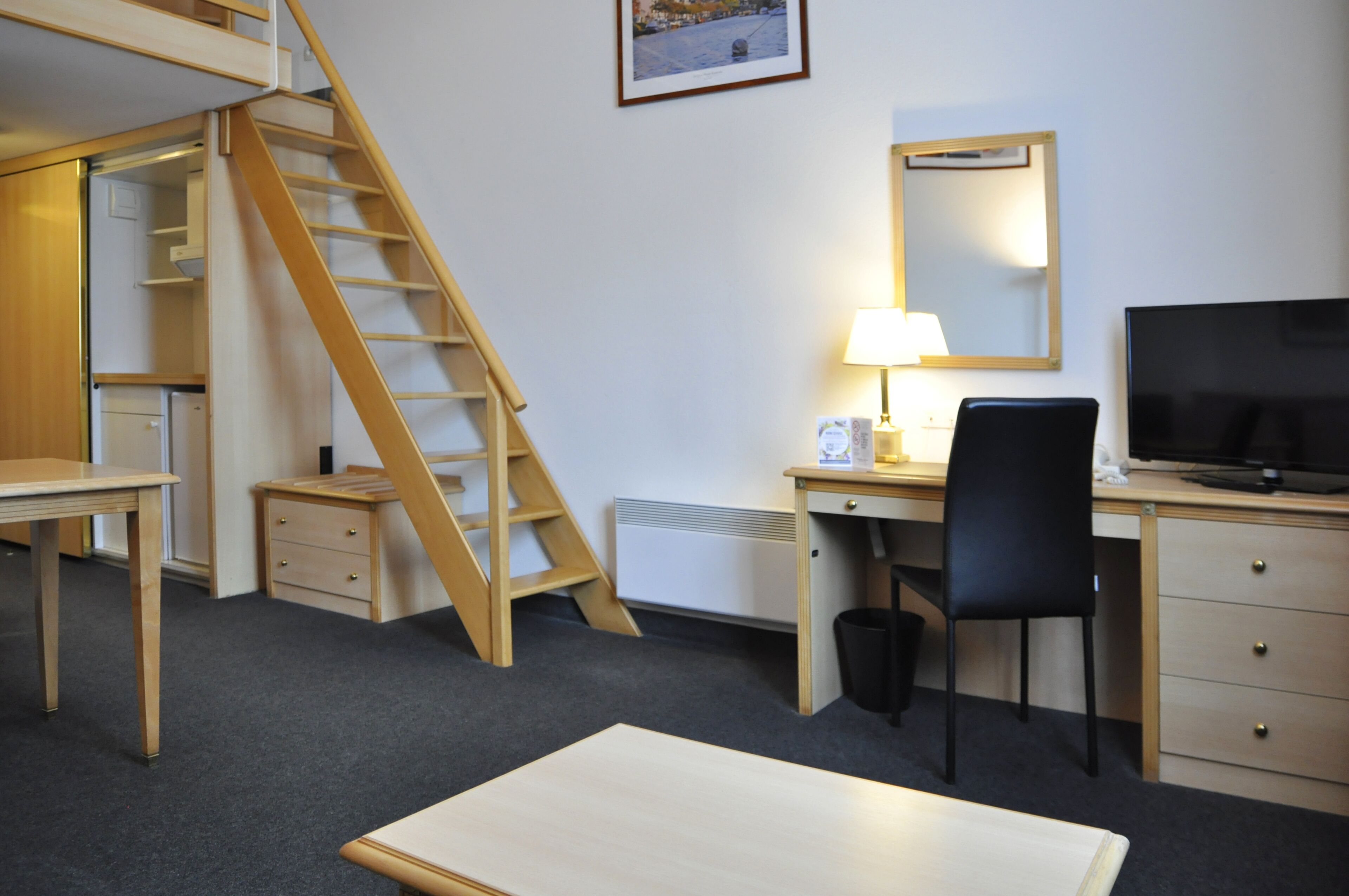 A room with a desk, chair, TV, lamp, and a wooden ladder.