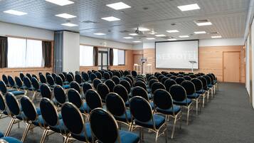 A conference room with rows of blue chairs, a projector screen, and a large screen displaying "WESTOTEL".
