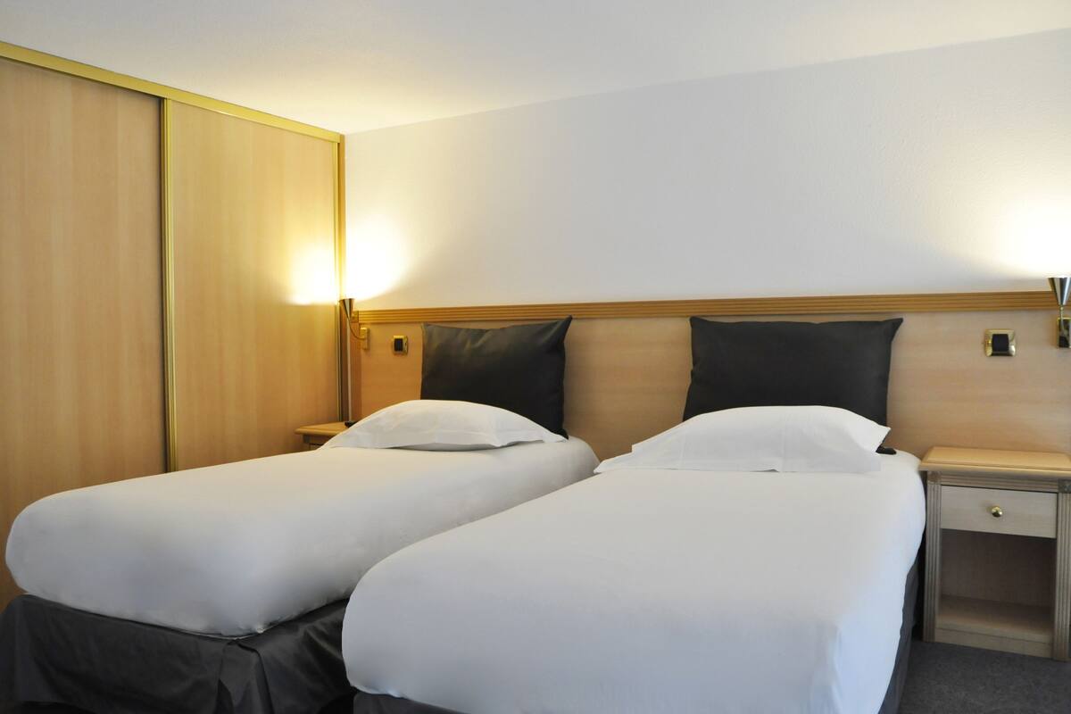 A hotel room with two single beds, a wooden headboard, bedside tables, and a wardrobe.