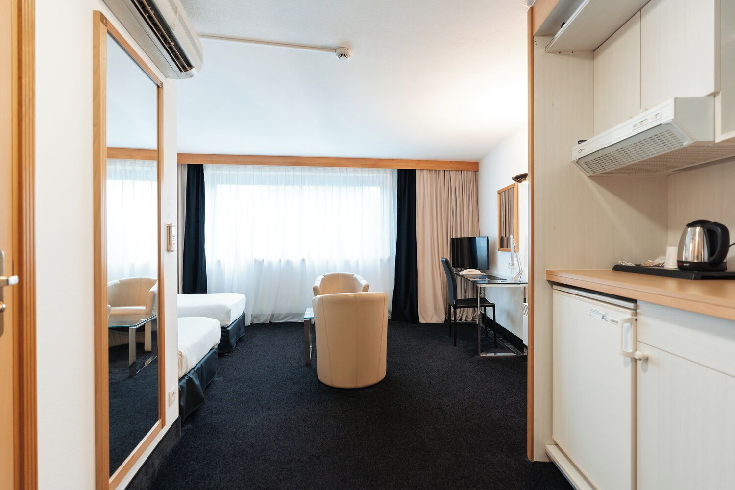 A hotel room with a bed, a desk with a chair, a television, a coffee maker, and a wardrobe.