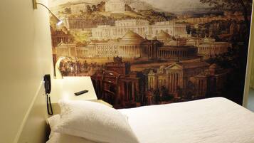 A hotel room with a bed, a lamp, and a wall mural of ancient architecture.