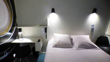 A hotel room with a bed, two bedside lamps, a desk with a chair, and a telephone.