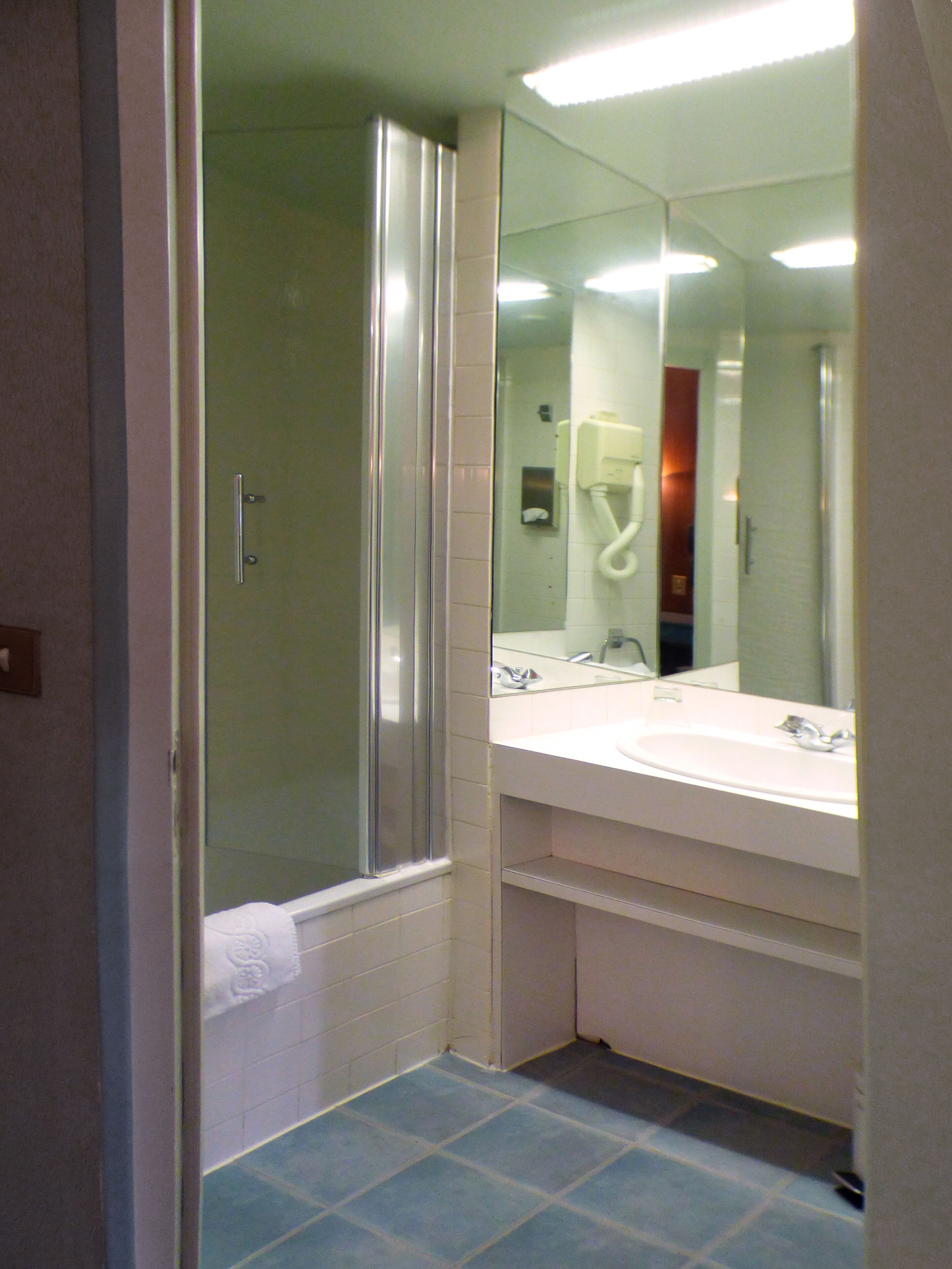 A bathroom with a glass-enclosed shower, a sink with a mirror, and a towel hanging on the wall.