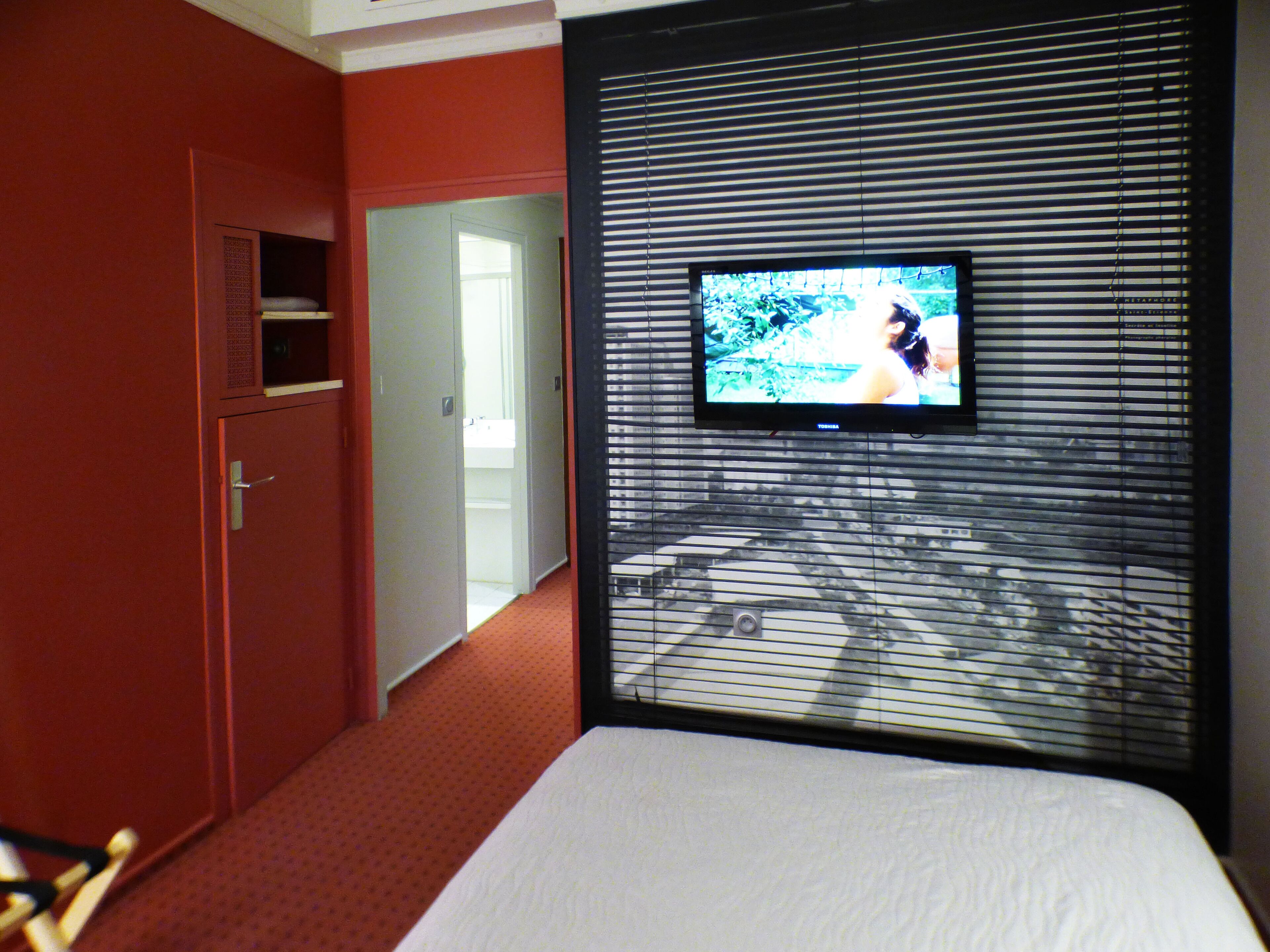 Una habitación de hotel con cama, televisión montada en la pared y puerta que da a otra habitación.
