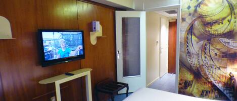 A hotel room with a television on a wooden cabinet, a bed, a small table, and a door leading to another room.