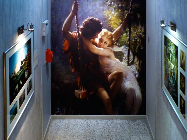 A corridor with a large painting of a woman on a swing.