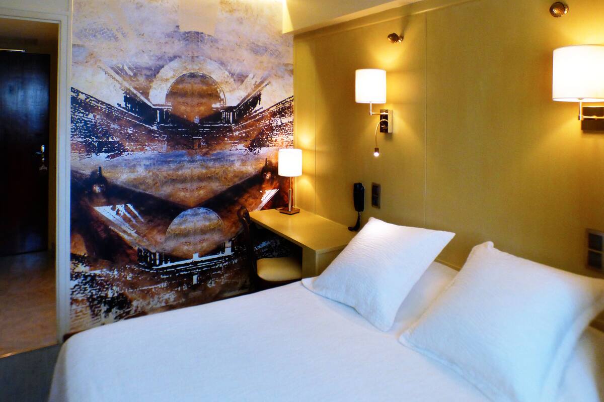 Una habitación de hotel con una cama grande, dos lámparas de noche, una mesita de noche y un mural en la pared.