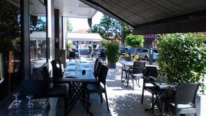 Un café en plein air avec des tables et des chaises, un espace de repos couvert et une vue sur la rue.