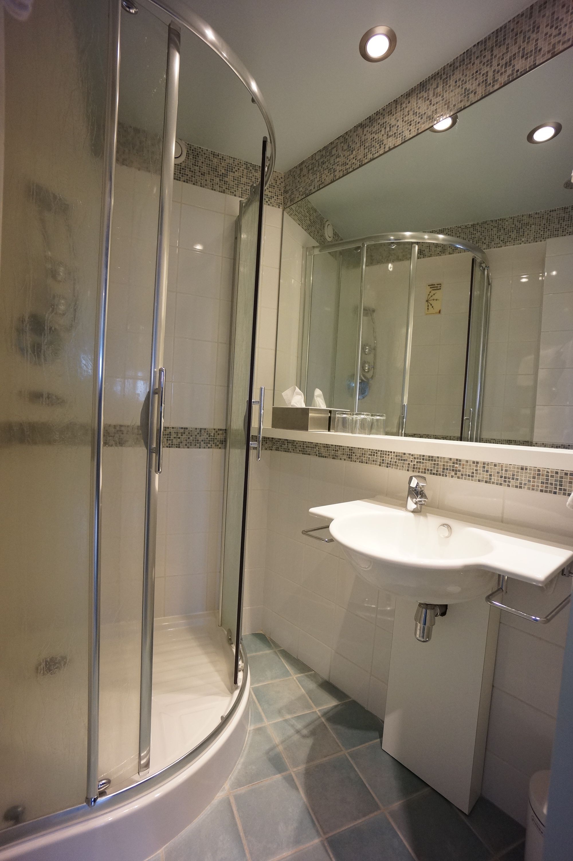 A modern bathroom with a glass-enclosed shower, a white sink, and a tiled floor.