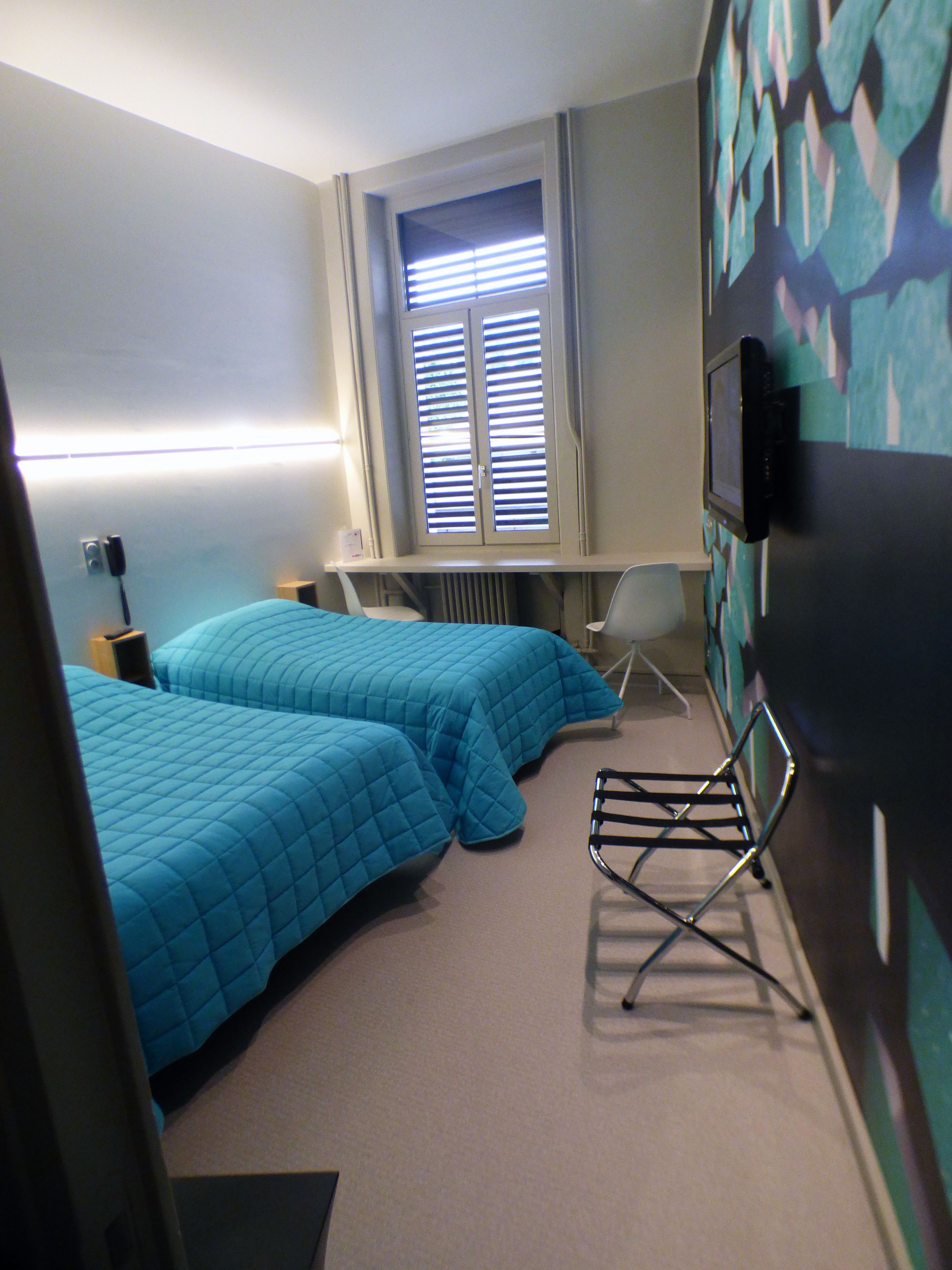 Habitación de hotel con dos camas, un escritorio, una silla, un radiador y un televisor.