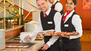 Een personeelslid van een hotel bedient eten bij een buffet met een glazen vitrine en een buffettafel.