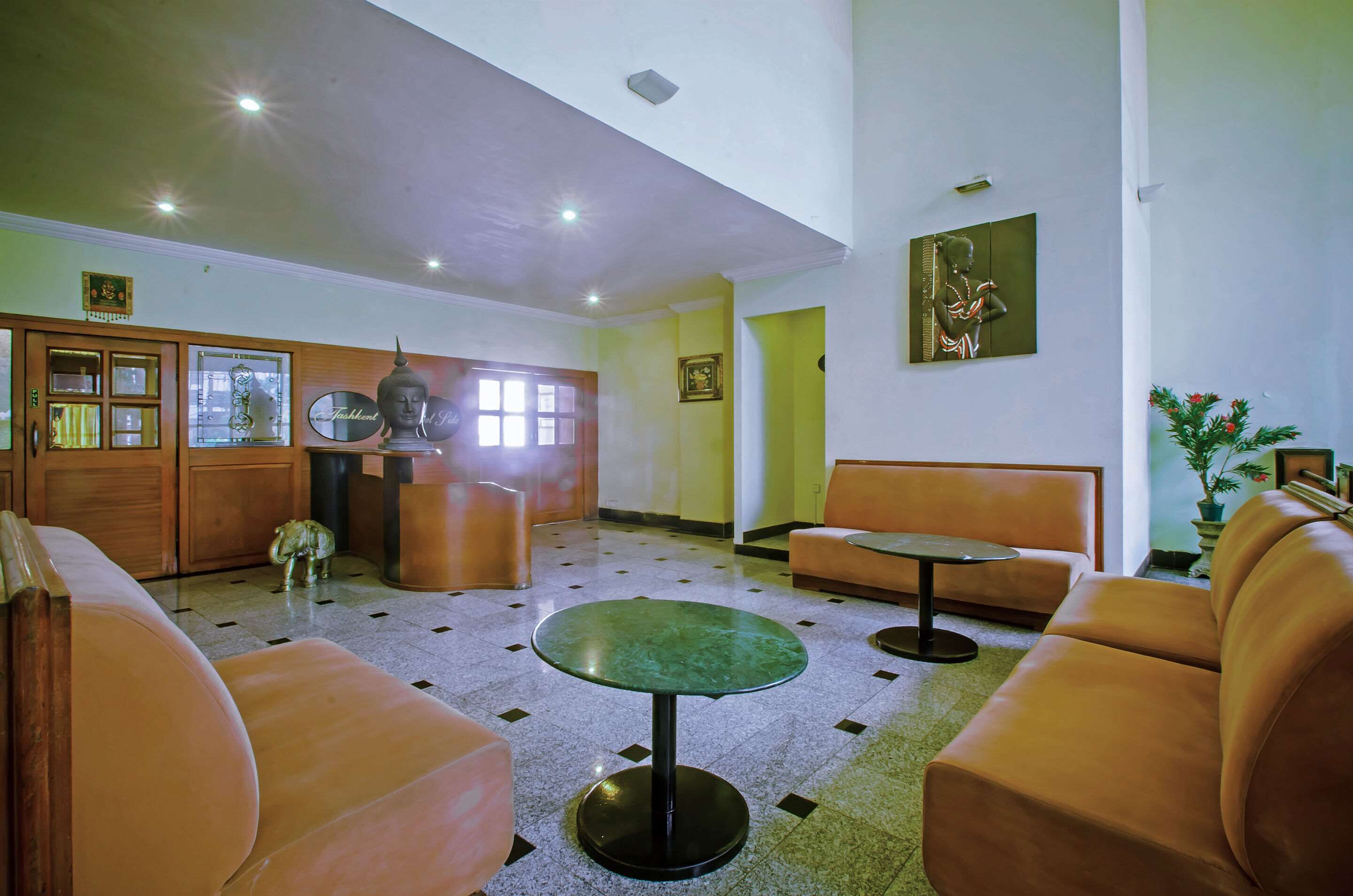 Un hall con una mesa redonda verde, sofás naranja, armarios de madera y una estatua de Buda.
