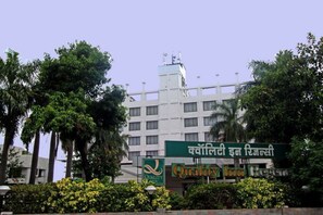A hotel with a sign in a local language and English, surrounded by greenery.