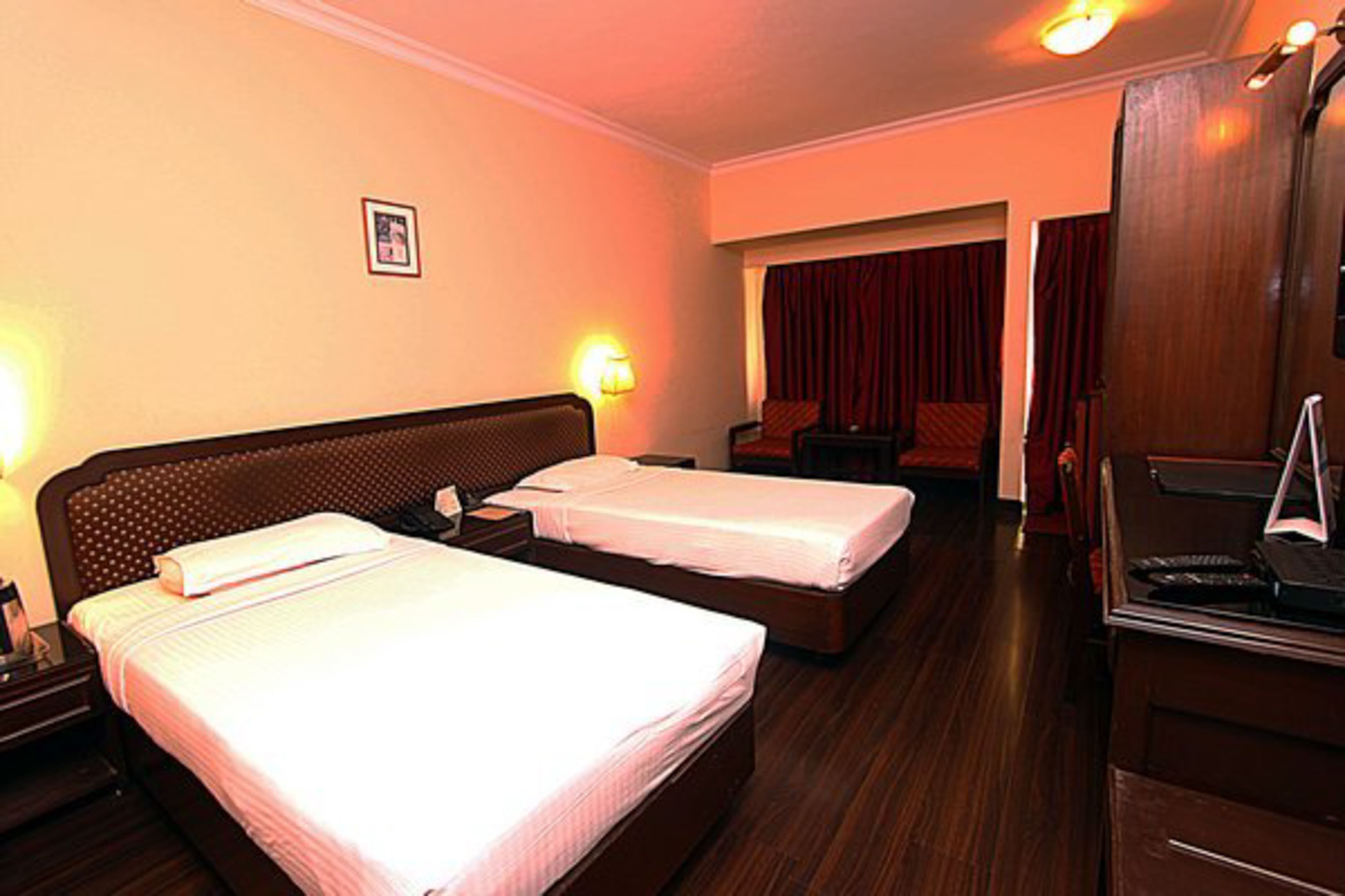 A hotel room with two beds, a desk, and a mirror.