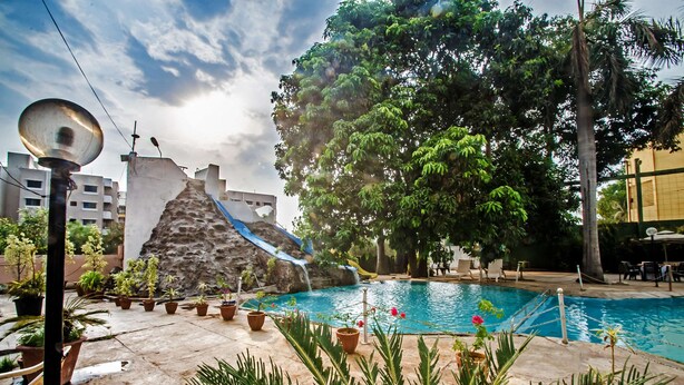A swimming pool with a waterfall feature, surrounded by potted plants and outdoor furniture.