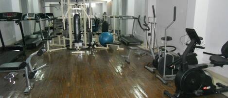 Un gimnasio con diversos equipos de ejercicio, incluyendo cintas de correr, una bicicleta estática y pesas sueltas.