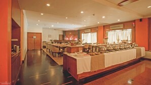 A buffet setup with a long table covered in a white tablecloth, surrounded by chairs and various food items.