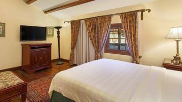 A hotel room with a large bed, a television, a desk with a lamp, and a window with curtains.