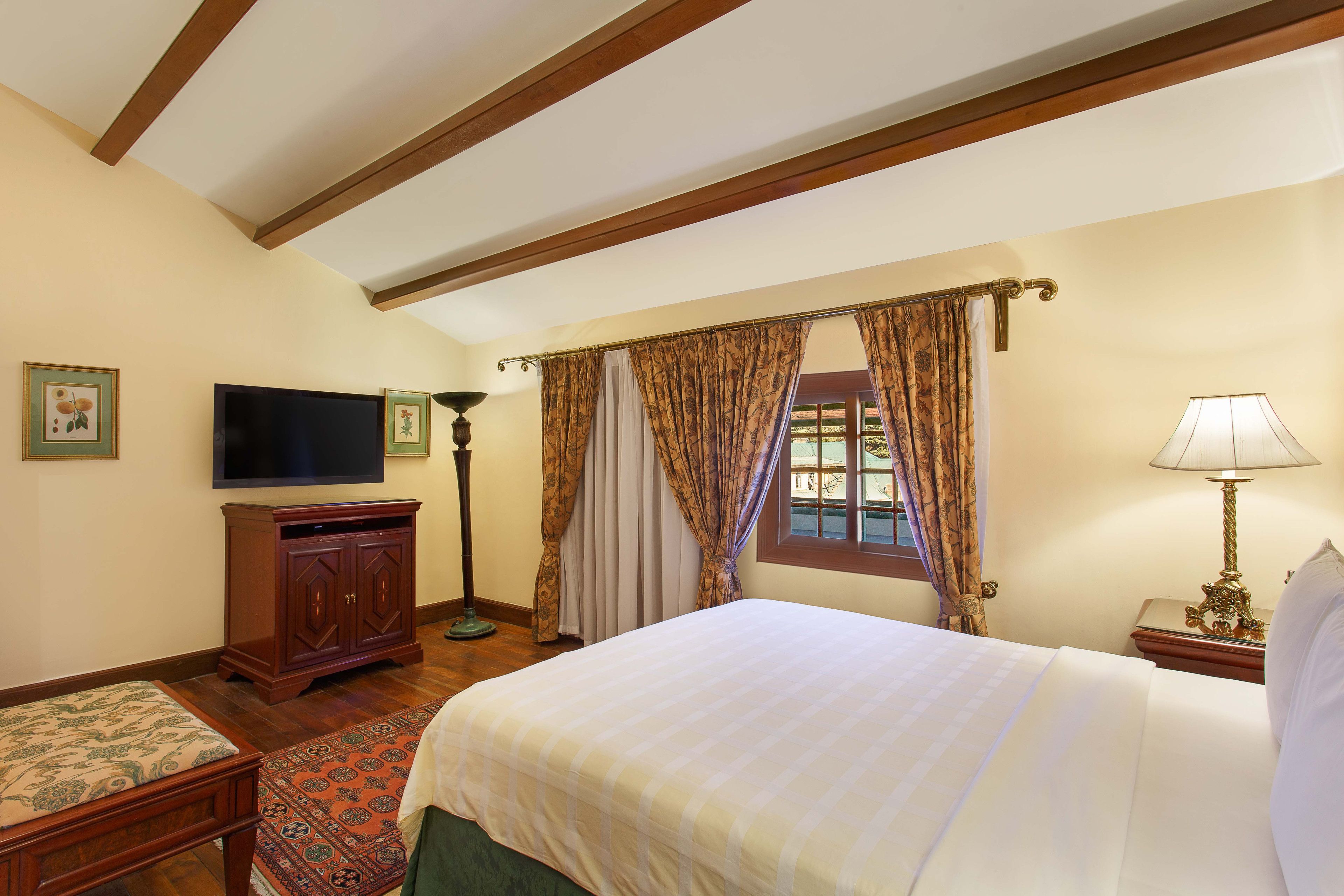 Une chambre d’hôtel avec un lit, une télévision, un bureau et une fenêtre avec des rideaux.