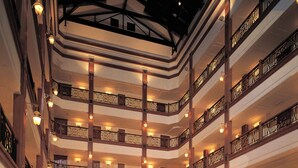 Un atrio de varios niveles con un espacio central abierto, amoblado con sofás, sillas y mesas, y con múltiples balcones con barandillas.