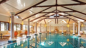 Una piscina interior con un diseño geométrico de azulejos, vigas de madera y columnas.