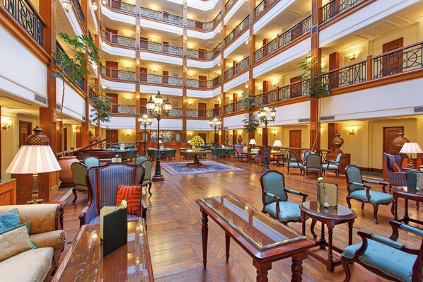 A multi-level hotel lobby with wooden floors, multiple seating areas, and a central chandelier.