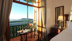 Habitación de hotel con balcón, una mesa de comedor con una bandeja de comida, una silla, una cama, una mesita de noche con lámpara y un espejo.
