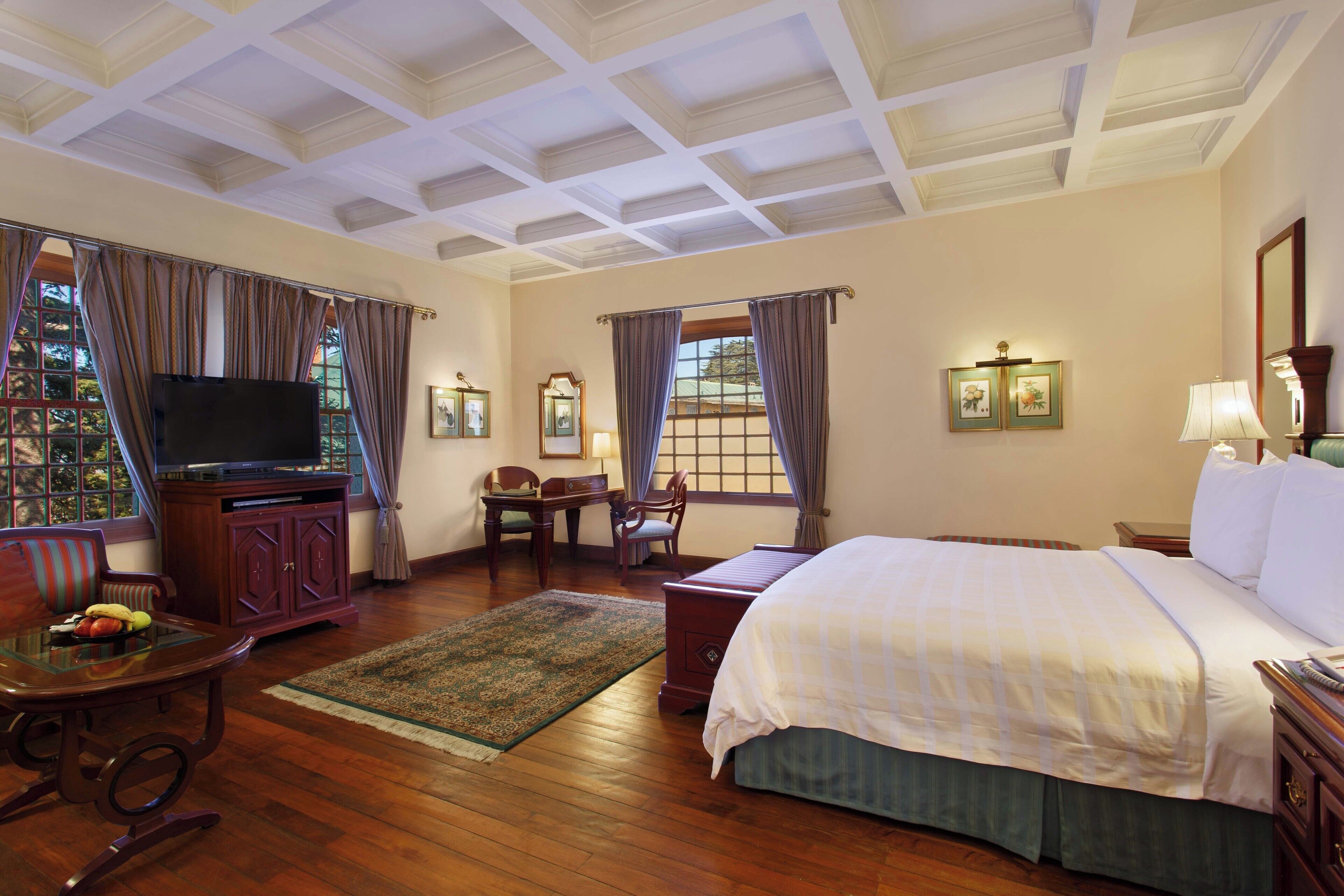 A hotel room with a large bed, a television, a desk with a chair, and a window with curtains.