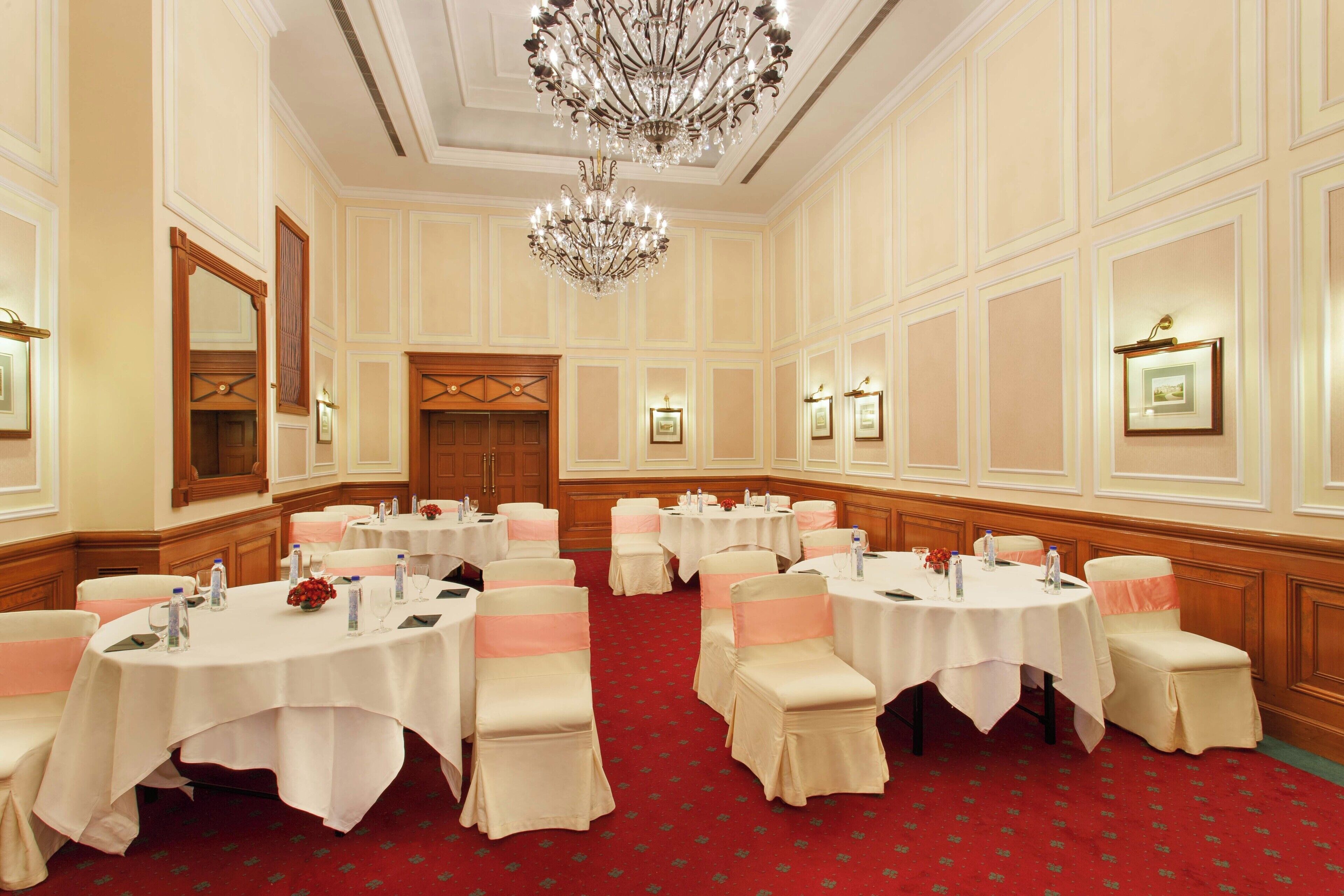 Une salle de banquet avec des tables rondes, des nappes blanches et des chaises ornées de rubans roses.