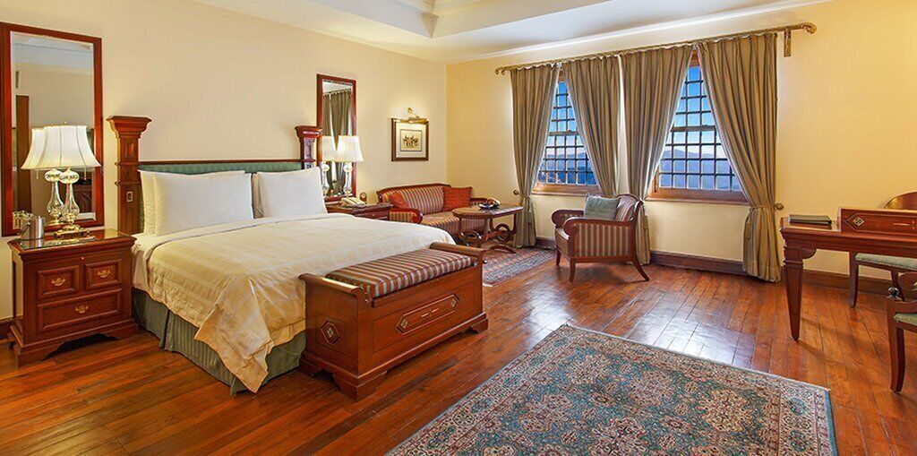 Habitación de hotel tradicional con una cama grande, un escritorio, una silla y una ventana con cortinas.