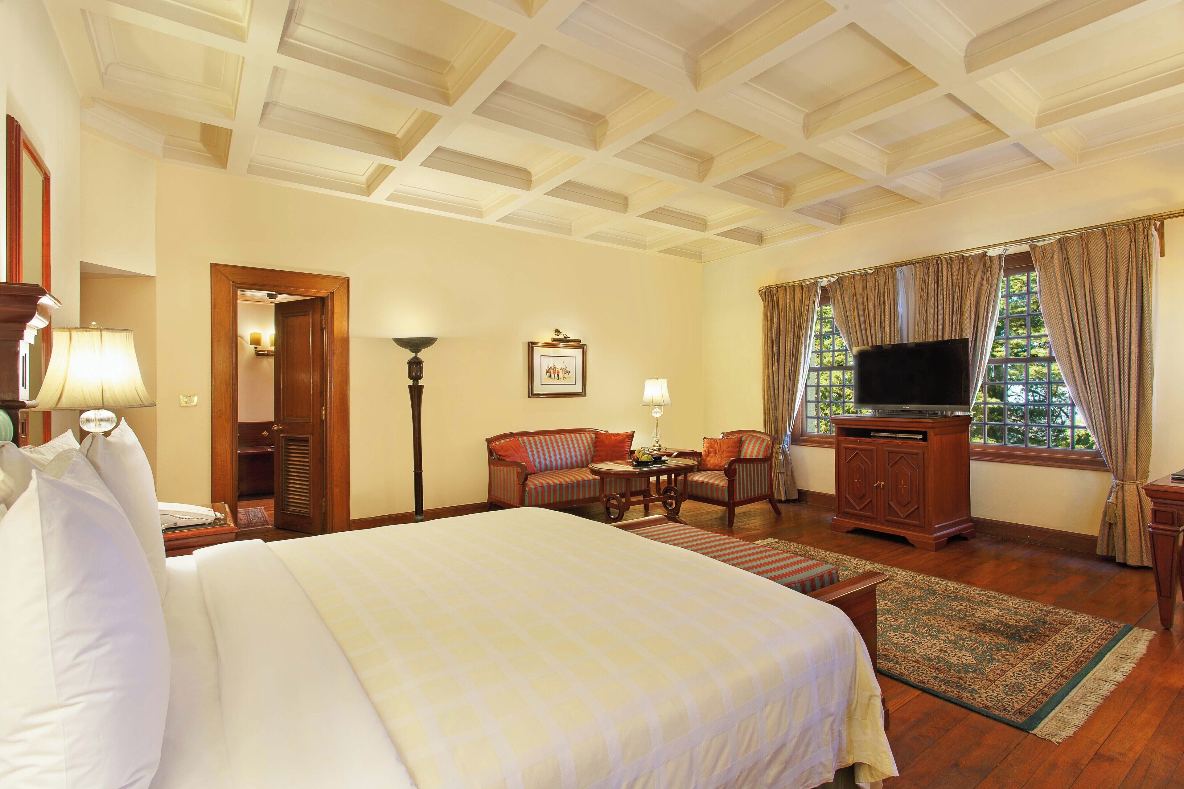 Una habitación de hotel con una cama grande, un escritorio con una silla, un televisor y una ventana con cortinas.
