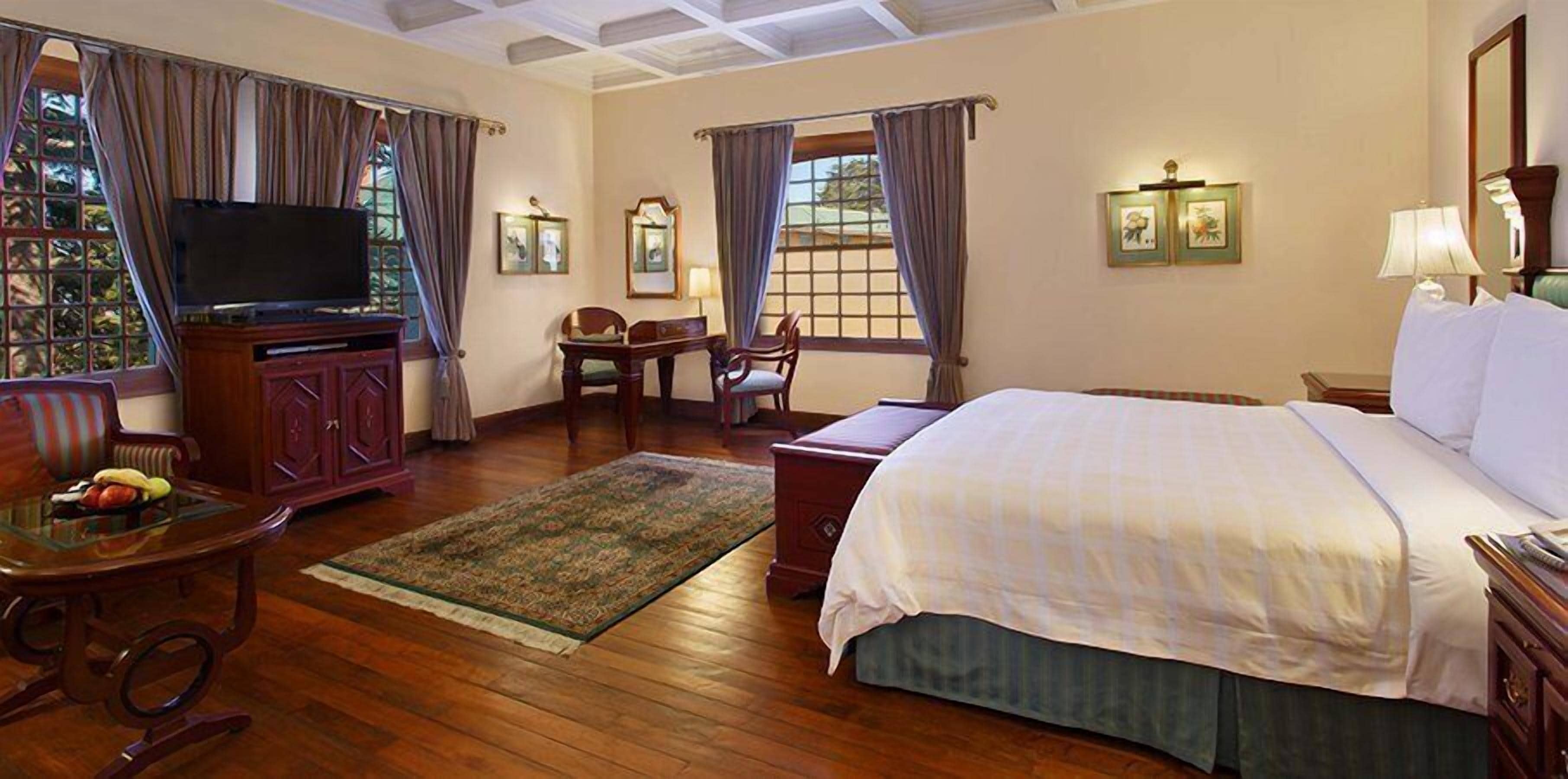 Una habitación de hotel con una cama, televisión, escritorio y una silla.