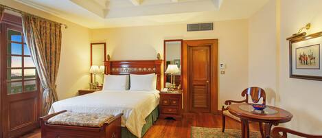 A traditional bedroom with a wooden bed, a small round table with a chair, a mirror, and a framed picture on the wall.